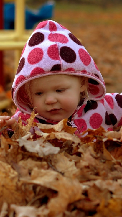 Dziewczynka bawi się w liściach jesienią