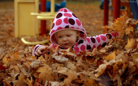 Tapeta Dziewczynka bawi się w liściach jesienią